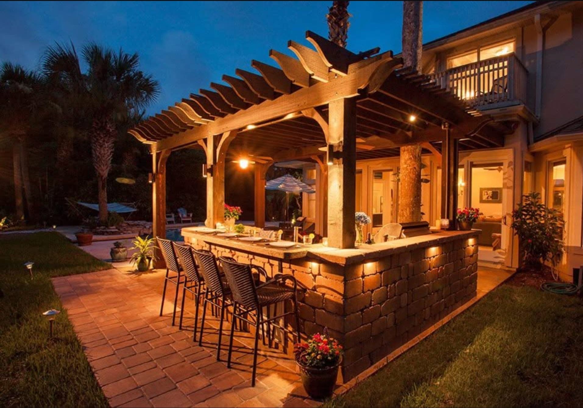 Paver seating area under a lit stone-columned pergola at twilight